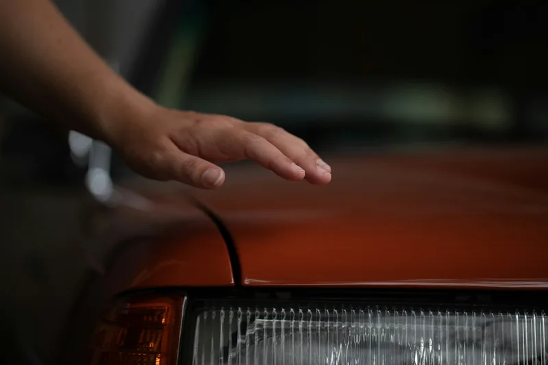 Hand prüft den Lack eines orangeroten Fahrzeugs